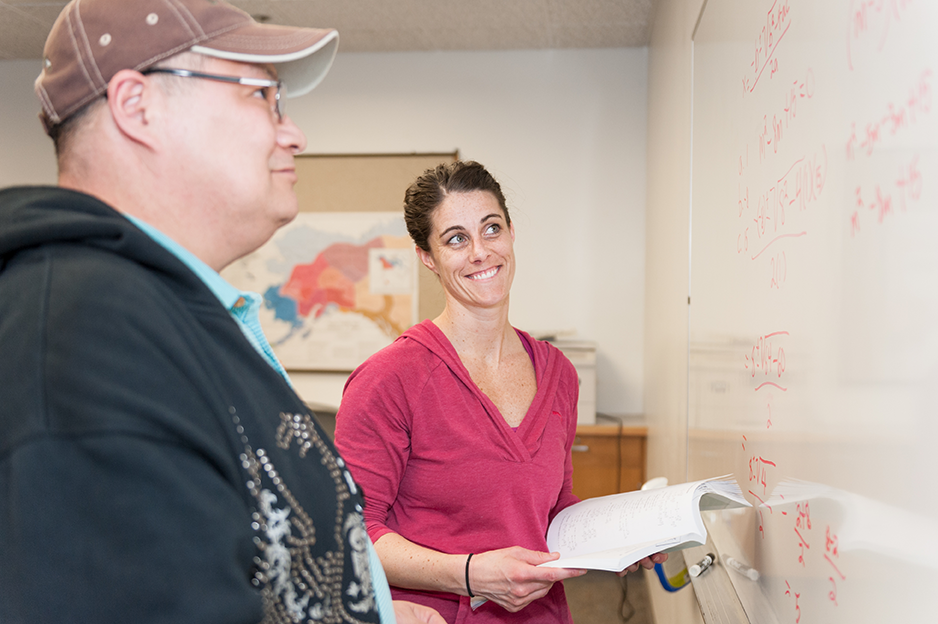 A tutor at a white board with a student looking on