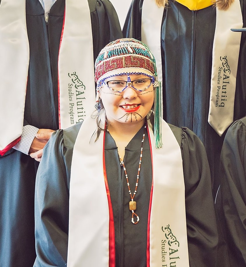 woman wearing a graduation gown and a ceremonial beaded alutiiq headdress