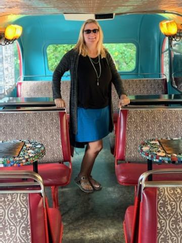 woman standing in a bus converted into an eating space with colorful benches and tables