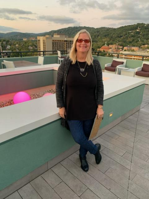Sue Buie standing on an urban rooftop with tree covered hills in the background