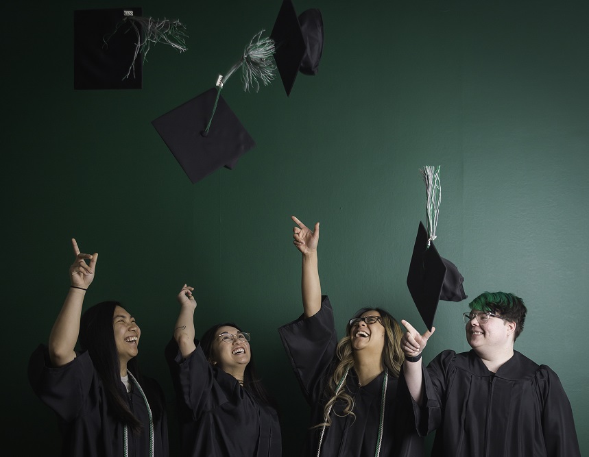 4 graduates throwing their caps in the air