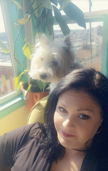 Jacelyn Keys seated on a couch in front of windows with a small white terrier behind her