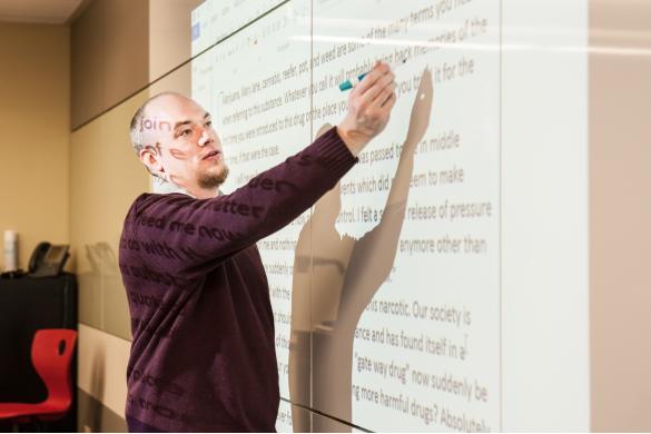 instructor writing on whiteboard with an essay projected