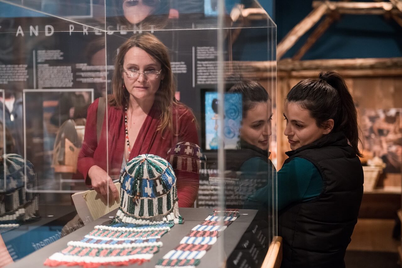 two women looking at an Alutiiq ceremonial headpiece in a glass case at the Alutiiq Museum