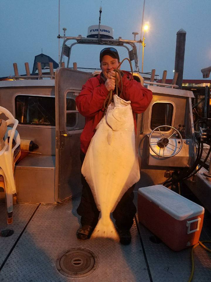 Kat Gambling holding a halibut on the back deck of a boat
