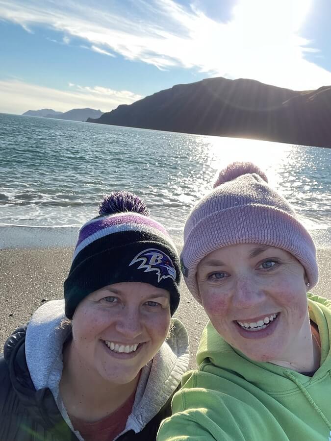 Kim saunders and kate karrow, wearing knit hats taking a selfie on the beach