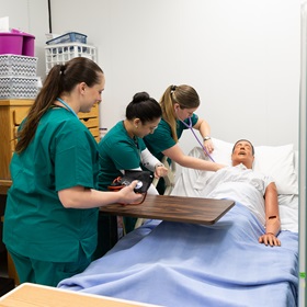 3 nursing students with a mannequin in a bed 