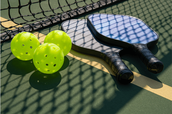 Pickleball paddles and balls on a court near a net