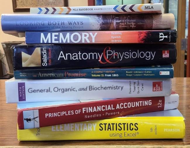 a stack of various college textbooks on a table