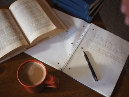 books, a pen, and a journal on a table with a cup of coffee