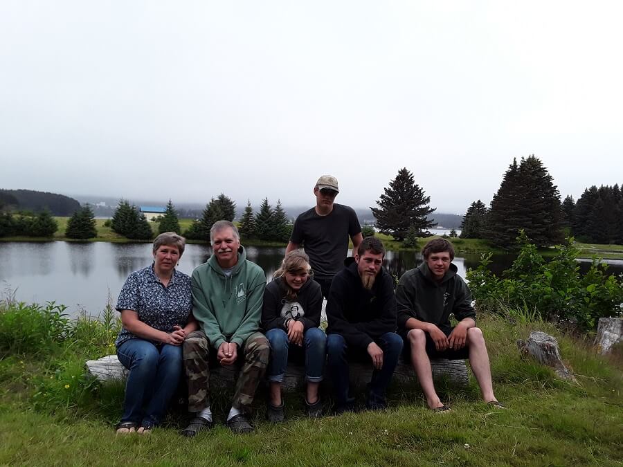 A family of 6 sitting outside on a log