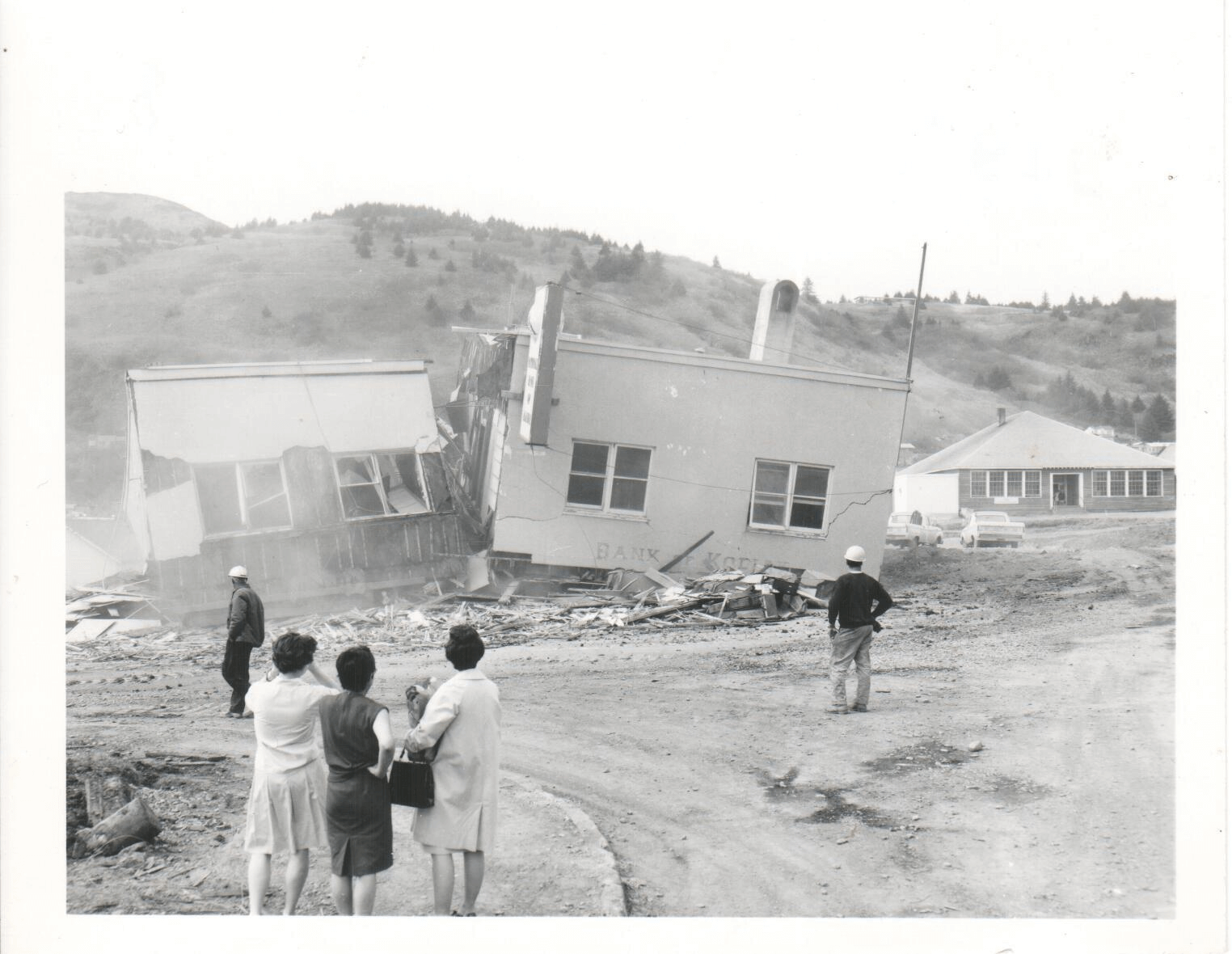 photograph of a damaged building in the process of being demolished with people watching