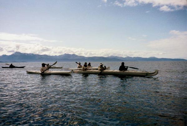 photograph of 4 single and one triple traditional kayaks on the ocean with people paddling