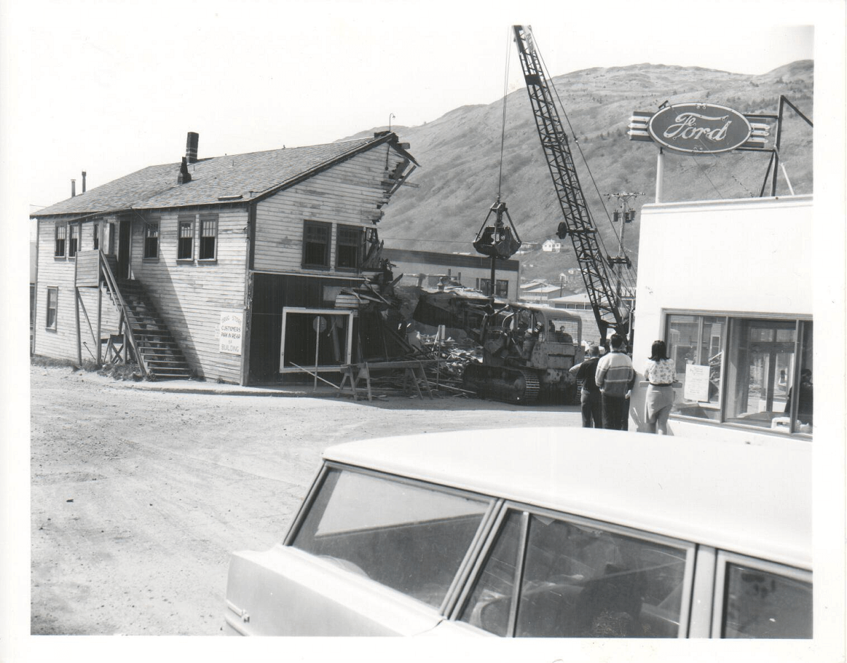 Photograph of onlookers watching a wooden building being demolished