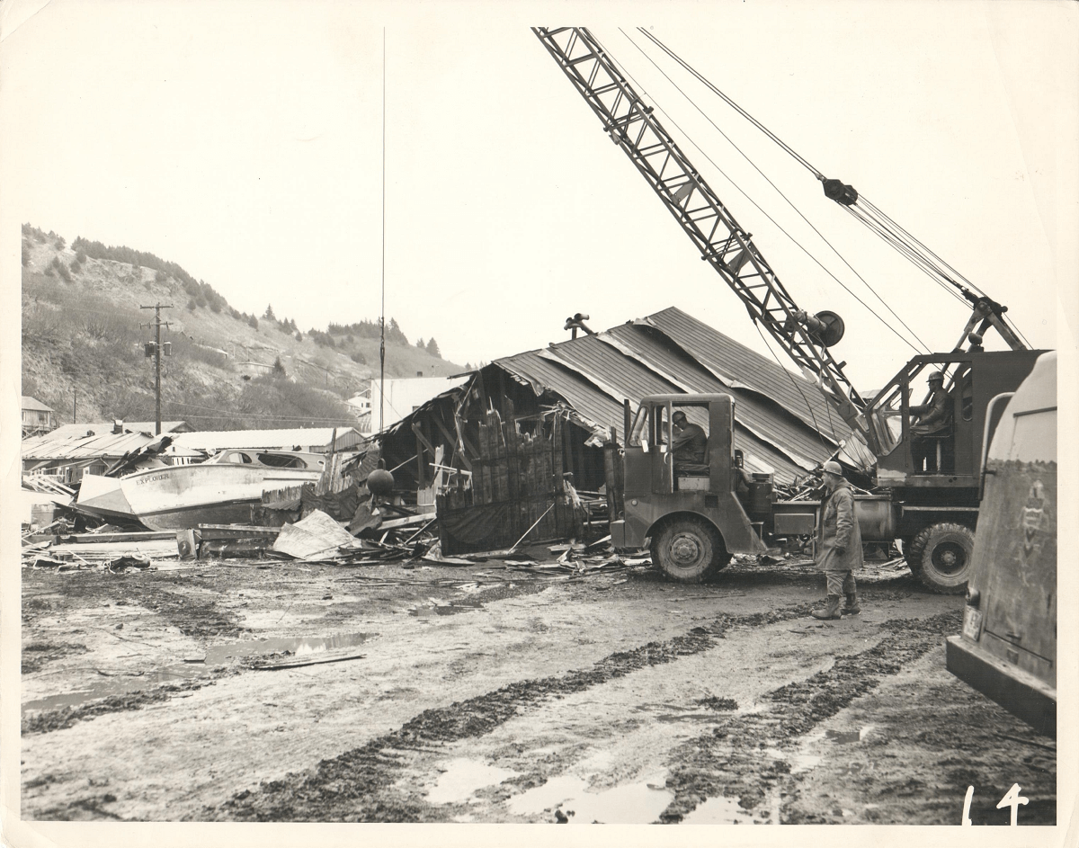 photograph of a crane and wrecking ball demolishing a wooden building with a soldier in the foreground